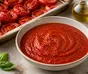 Skål med glat rød tomatsauce omgivet af ovnbagte tomater, hvidløg og basilikum
